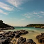 a beach with rocks and water under a blue sky