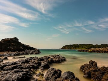 a beach with rocks and water under a blue sky